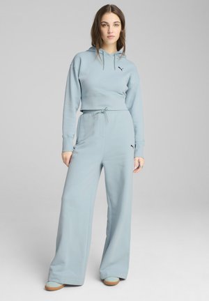 Felpa corta azzurro chiaro con cordino, abbinata a pantaloni a gamba larga. Entrambi hanno una texture morbida e accenti del logo neri.