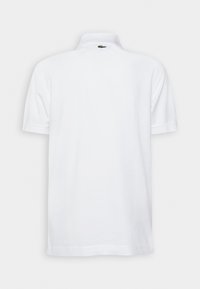 Hvit polo-shirt med brettet krage, korte ermer, og en liten grønn logo på baksiden nær nakken. Myk bomullstekstur.