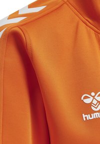Orange sweatshirt med en glat tekstur, høj krave og hvide logo- og chevron-detaljer på skuldrene.