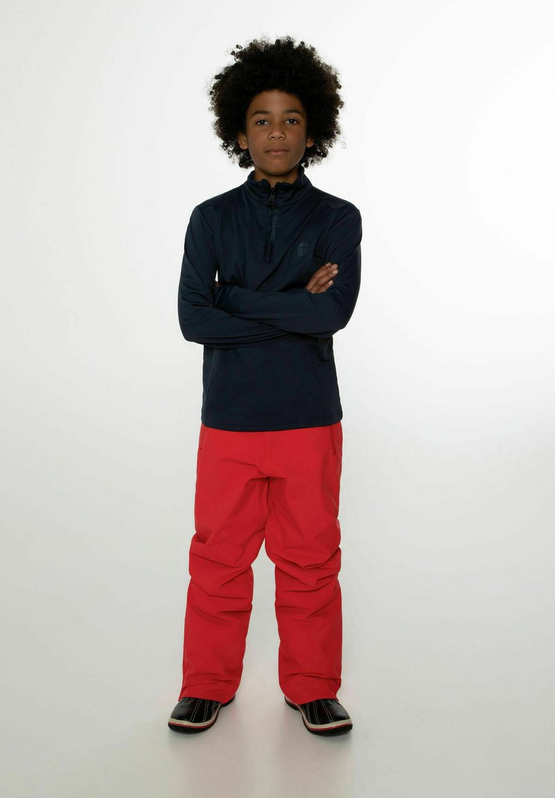 Maglione zip-up a maniche lunghe blu scuro abbinato a pantaloni da neve rossi brillanti. L'insieme presenta una texture liscia e una vestibilità casual. Inclusi calzature nere.