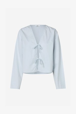 Hele sinine lühike pluus pikkade varrukatega, V-dekoltee ja ees nööriga sulgemisega. Valmistatud siledast kangast, millel on veidi struktureeritud tekstuur.