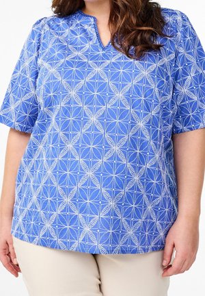 Blouse bleue à manches courtes avec un motif géométrique blanc, décolleté en V et détails froncés aux épaules. Tissu léger.