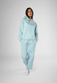 Sudadera azul claro y joggers a juego, hechos de tela suave, con letras plateadas y adornos en las mangas. Zapatillas blancas.