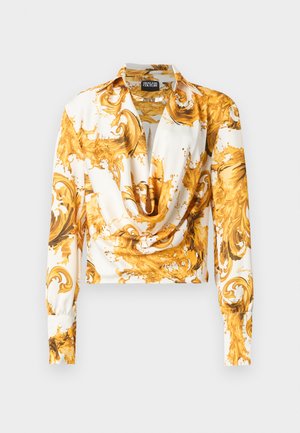 Balta blūze ar garām piedurknēm, zeltainu greznu baroka rakstu un drapētu cowl izgriezumu, ar Versace Jeans Couture etiķeti.