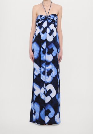 Robe longue sans bretelles avec motif floral abstrait bleu, noir et blanc, portée avec une bretelle de cou halter torsadée.