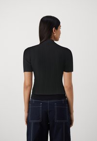 Sort ribbet t-shirt med korte ærmer, høj krave, tætsiddende design og tekstureret stof. Bagfra viser det en strømlinet og moderne silhuet.