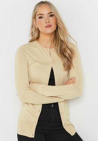 Cardigan beige à manches longues avec un col rond, fermeture à boutons et poignets côtelés. Texture douce, design ajusté et léger éclat.