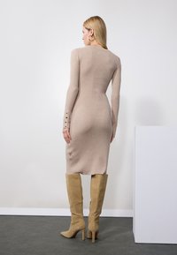 Beige ribbet kjole med lange ermer og knapdetaljer ved manchetterne, kombinert med beige semsket skinnstøvler til knærne, sett fra baksiden.