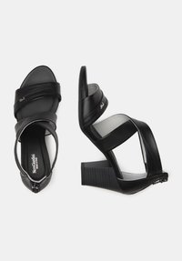 Sorte højhælede sandaler med læderremme og en tekstureret blokhælt. Har en lynlåslukning og et buet overdesign for ekstra stil.