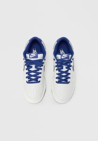 Sneakersy Nike z białą skórzaną cholewką, niebieskimi akcentami, okrągłym noskiem, perforowanymi detalami i niebieskimi sznurowadłami. Podeszwa jest płaska i wykonana z gumy.