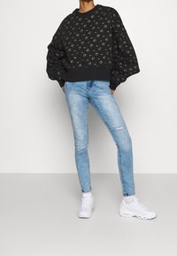 Černá mikina se zlatým kruhovým vzorem, nadýchané rukávy, spárována se světle modrými roztrhanými skinny džíny a bílými teniskami.