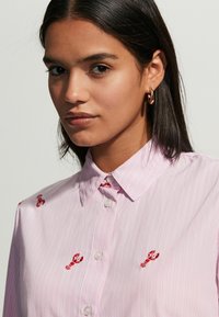 Pink striped button-up shirt featuring red lobster embroidery, with a structured collar and smooth fabric texture.