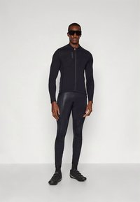 Completo atletico nero composto da una maglia aderente a maniche lunghe con cerniera frontale e leggings abbinati, realizzati in tessuto liscio ed elastico.