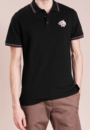 Czarna koszulka polo wykonana z bawełny, z logo tygrysa na lewej piersi. Kołnierz i rękawy mają kontrastowe czerwone i białe paski.