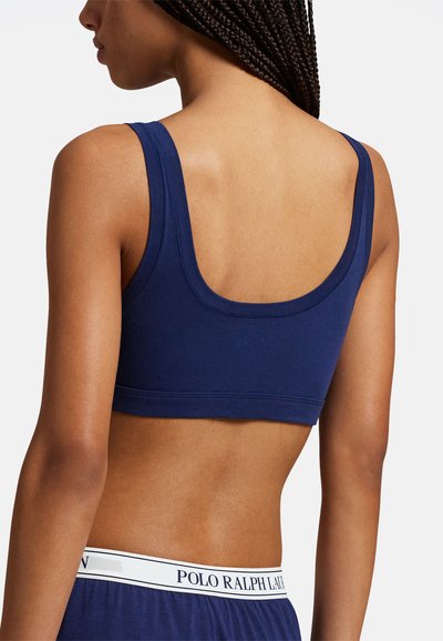 Tmavě modrá bavlněná sportovní podprsenka s výstřihem na zádech do tvaru lžíce, širokými ramínky a elastickým pruhem s logem. Hladká textura bez vzorů.