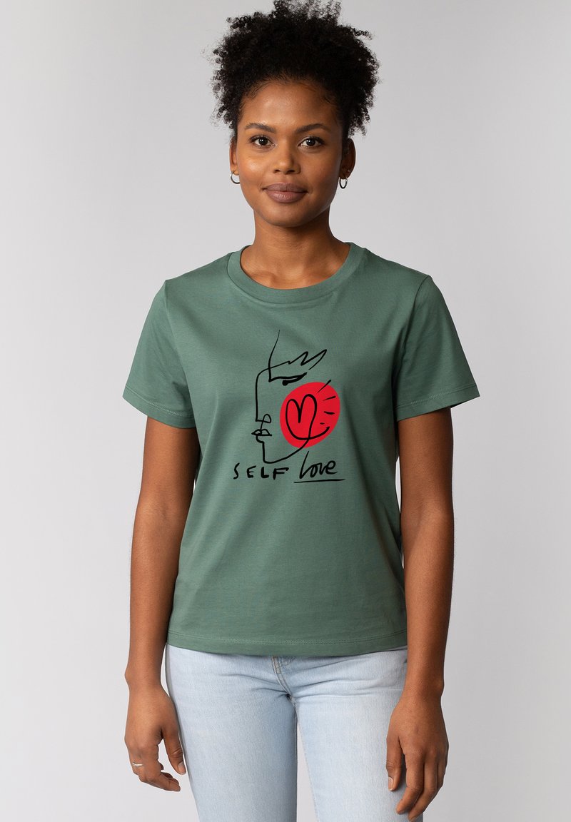Groene katoenen T-shirt met een zwarte lijntekening van een gezicht, een rood hart en de tekst "SELF love" in het zwart. Korte mouwen en ronde halslijn.