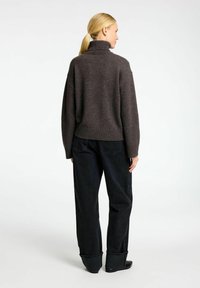 Tmavě šedý oversized svetr s vysokým límcem, texturovaným pletením a žebrovaným lemem, doplněný černými džíny s vysokým pasem. Jednoduchý, čistý design.