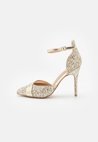 Glittering gold high-heeled shoe with pointed toe, ankle strap, and metallic accents. Features a textured glitter surface and shiny finish.