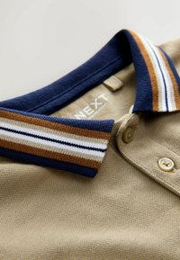 Polohemd aus braunem Stoff mit strukturierter Oberfläche, ausgestattet mit einem navyfarbenen Kragen mit braunen und weißen Streifen sowie zwei Knöpfen auf der Vorderseite.