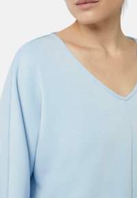 Lichtblauwe V-hals top van zachte stof met een relaxte pasvorm en licht oversized mouwen; heeft een eenvoudige naaddetail langs de halslijn.