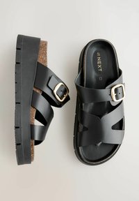 Sorte platform sandaler med brede krydsseler, en kork mellemsål og en gylden spænde detalje. Tekstureret sort gummisål for bedre greb.