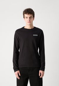 Melnā garām piedurknēm krekls, izgatavots no mīkstas auduma, ar apaļu kakla izgriezumu un mazu Calvin Klein logotipa uzšuvumu kreisajā augšējā krūšu daļā.