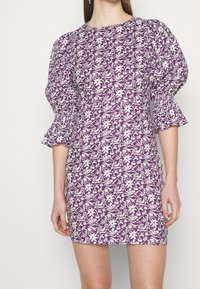 Robe mini florale violette avec manches bouffantes, ornée de motifs botaniques blancs et de poignets élastiques pour un effet texturé.