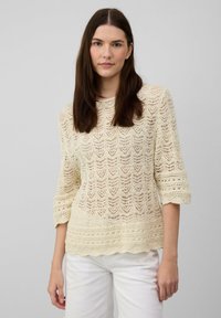 Sweter dzianinowy w odcieniu off-white z koronkowym wzorem, rękawami o długości trzech czwartych, falbaniastym dołem i lekką teksturą, połączony z białymi dołami.