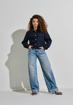 Marineblauwe cropped jas met twee voorzakken en witte knopen, gecombineerd met lichtblauwe wide-leg jeans en leopardenprint hakken.