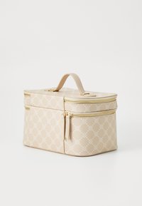 Ljust beige kosmetikväska med texturerad yta, gyllene dragkedjor och ett handtag på toppen. Har ett geometriskt mönster i vitt över hela ytan.