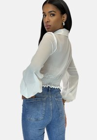 Witte, doorschijnende blouse met lange mouwen, geplooide taille, zachte textuur en uitlopende manchetten, gecombineerd met hoge taille blauwe spijkerbroek met achterzakken.