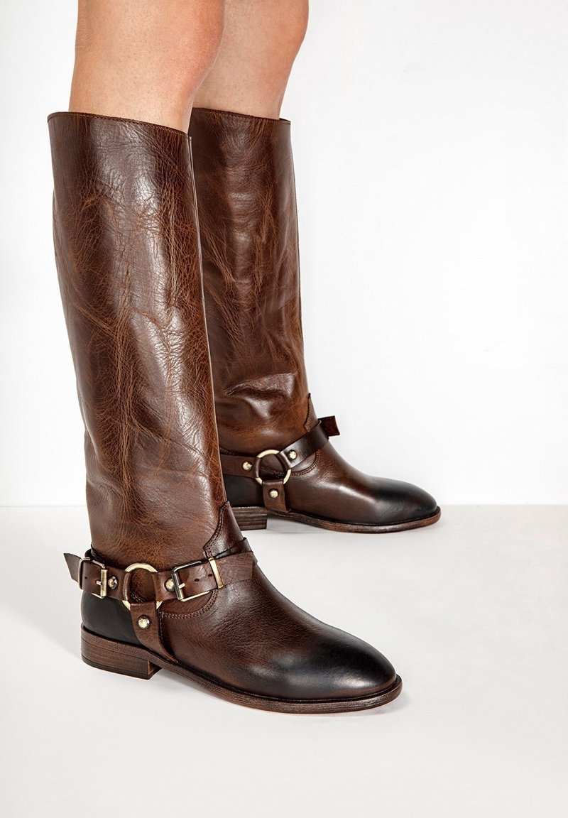 Bottes montantes en cuir marron à finition texturée, avec des boucles et accents en métal, et un bout noir contrastant.