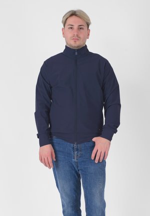 Giacca navy con colletto alto e zip completa, dotata di maniche lunghe e design aderente, abbinata a jeans di jeans leggero blu.