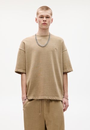 Khaki oversized tričko vyrobené z mäkkej tkaniny, s poklesnutými plecami, okrúhlym výstrihom a jemným logom; v kombinácii s kuklovými šortkami.