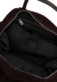Brown suede bag interior with a black lining, featuring a zip pocket and a brand tag, has a smooth texture and silver zipper hardware.