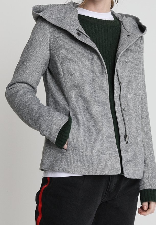 Grijze gewatteerde jas met een gestructureerde stof, voorzien van een ritssluiting, zakken en geribbelde groene gebreide manchetten. Zwarte broek met rode strepen.