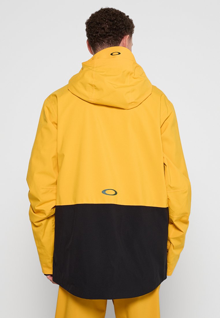 Giacca impermeabile gialla e nera con cappuccio, caratterizzata da una texture liscia e un dettaglio del logo vicino all'orlo. La lunghezza scende sotto la vita.