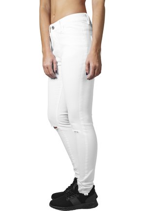 Biele skinny džínsy s poškodeným dizajnom, ktoré majú roztrhnutia na kolenách a vysoký pás. Skombinované s čiernymi športovými teniskami.
