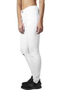 Jeans skinny blancos con un diseño desgastado que presenta roturas en las rodillas y una cintura alta. Combinados con zapatillas deportivas negras.