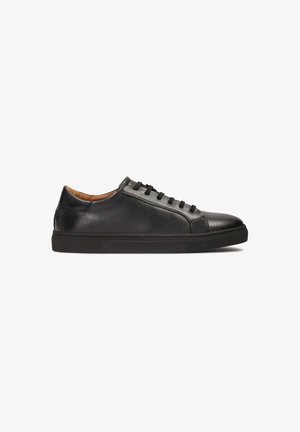 Zapatilla negra de cuero con textura suave, puntera redondeada, cinco ojales y un forro marrón de contraste. Suela de goma para un buen agarre.