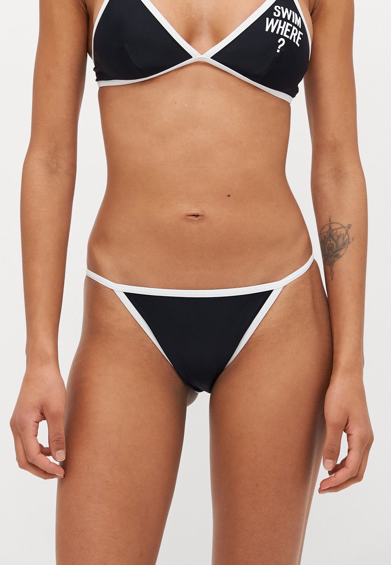 Juodas bikini komplektas, kuriame yra trikampis liemenėlė ir minimaliai uždengiantys apatiniai, papuošti baltais kraštais ir tekstiniu motyvu ant viršaus.
