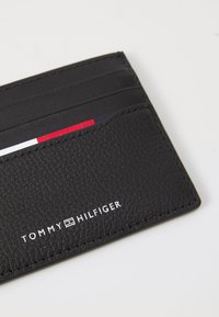 Black leather cardholder featuring textured finish, five card slots, and embossed "TOMMY HILFIGER" logo in white at the bottom.