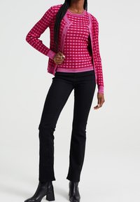 Rosa rutigt långärmad tröja över matchande topp, tillsammans med svarta tighta byxor och blockklackade ankelstövlar. Sl ät textur.