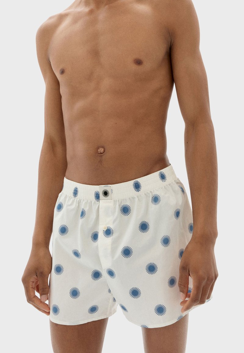 Weiße Baumwollboxershorts mit blauen Kreismustern, elastischem Bund und vorderer Knopfverschluss. Weiche Textur und lockere Passform.