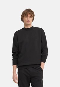 Sudadera negra con cuello redondo, tejido texturizado y discreto detalle del logo en el pecho. Presenta puños y dobladillo acanalados.