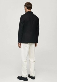 Blazer negru, pantaloni albi, material neted, croială ajustată, linii clare, design minimalist, vedere din spate, asortat cu pantofi negri.
