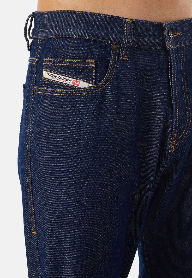 Dunkelblaue Denim-Jeans mit geradem Schnitt, orangefarbenen Nähten und einem Logo-Patch auf der Gesäßtasche. Metallknopf an der Taille.