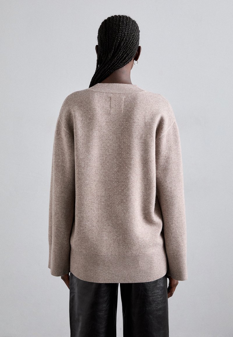 Beiger oversize Pullover mit strukturierter Oberfläche, ausgestattet mit einem gerippten Saum und Bündchen. Einfaches Design mit einem dezenten, offenen Halsausschnitt und Rückennahtdetails.