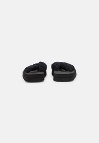 Black slippers with plush, textured upper, wide straps, and rubber soles. The design features a soft, fuzzy finish and a contoured shape.