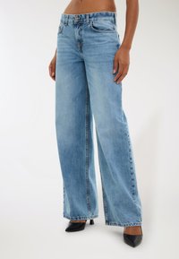 Jeans ampi di colore azzurro realizzati in denim, con chiusura a bottone e cerniera, tasche anteriori e orli sfrangiati. Abbinati a tacchi neri.